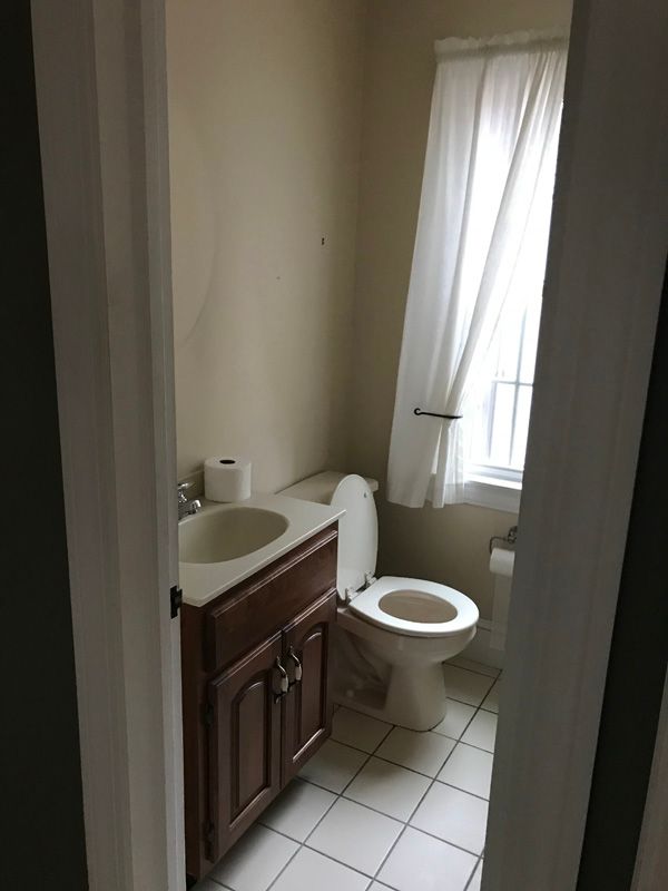 Small bathroom with sink vanity, toilet, white tile floor, and a window with sheer curtains.