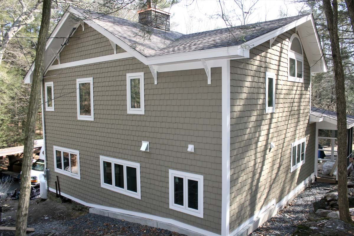 Tan-sided two-story house with white trim and multiple windows among trees