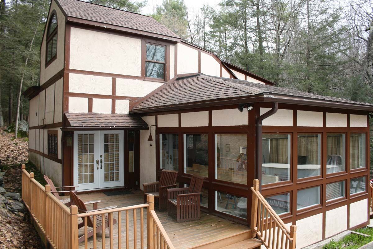 Two-story house with brown trim, a covered porch, and large windows in a wooded setting