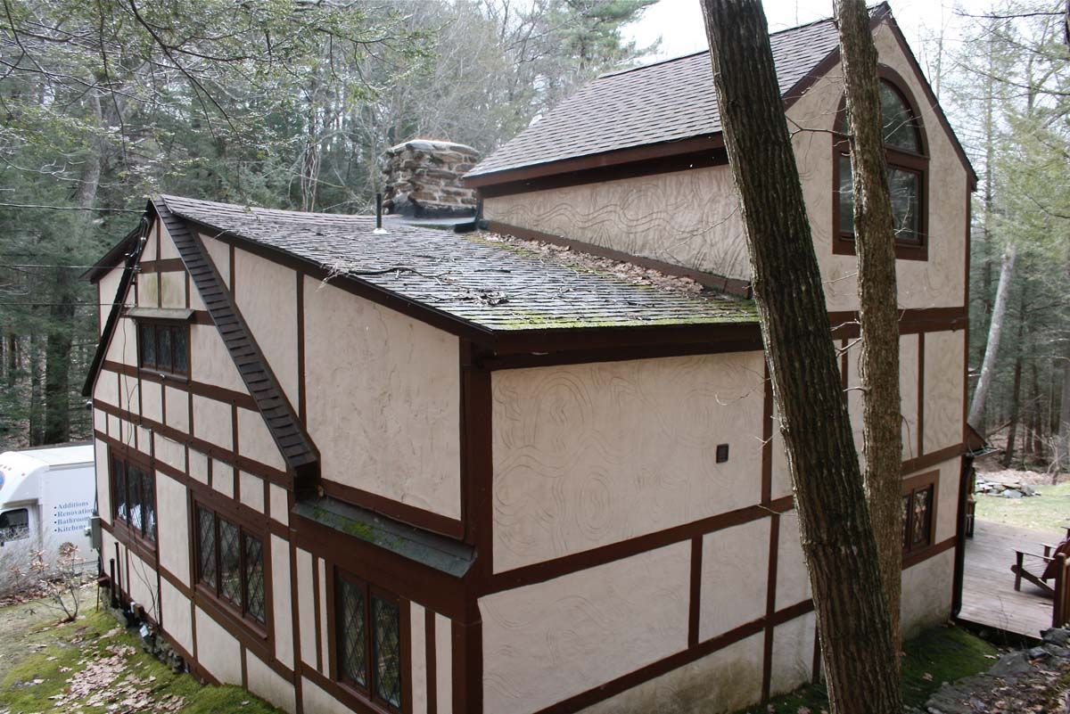Tudor-style house with tan walls and dark timber framing in a wooded area.