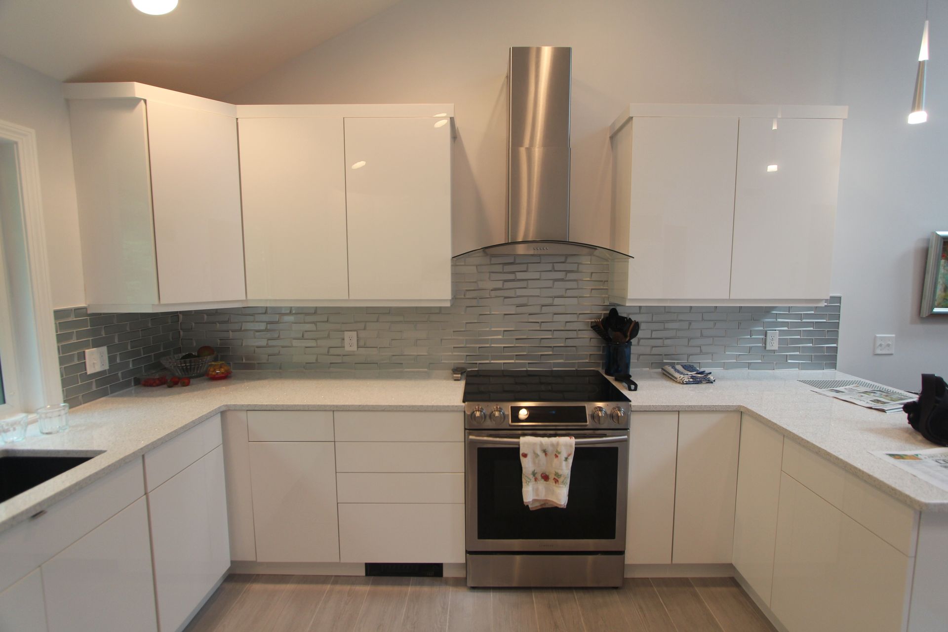 Modern white kitchen with stainless steel range hood, stove, and tiled backsplash