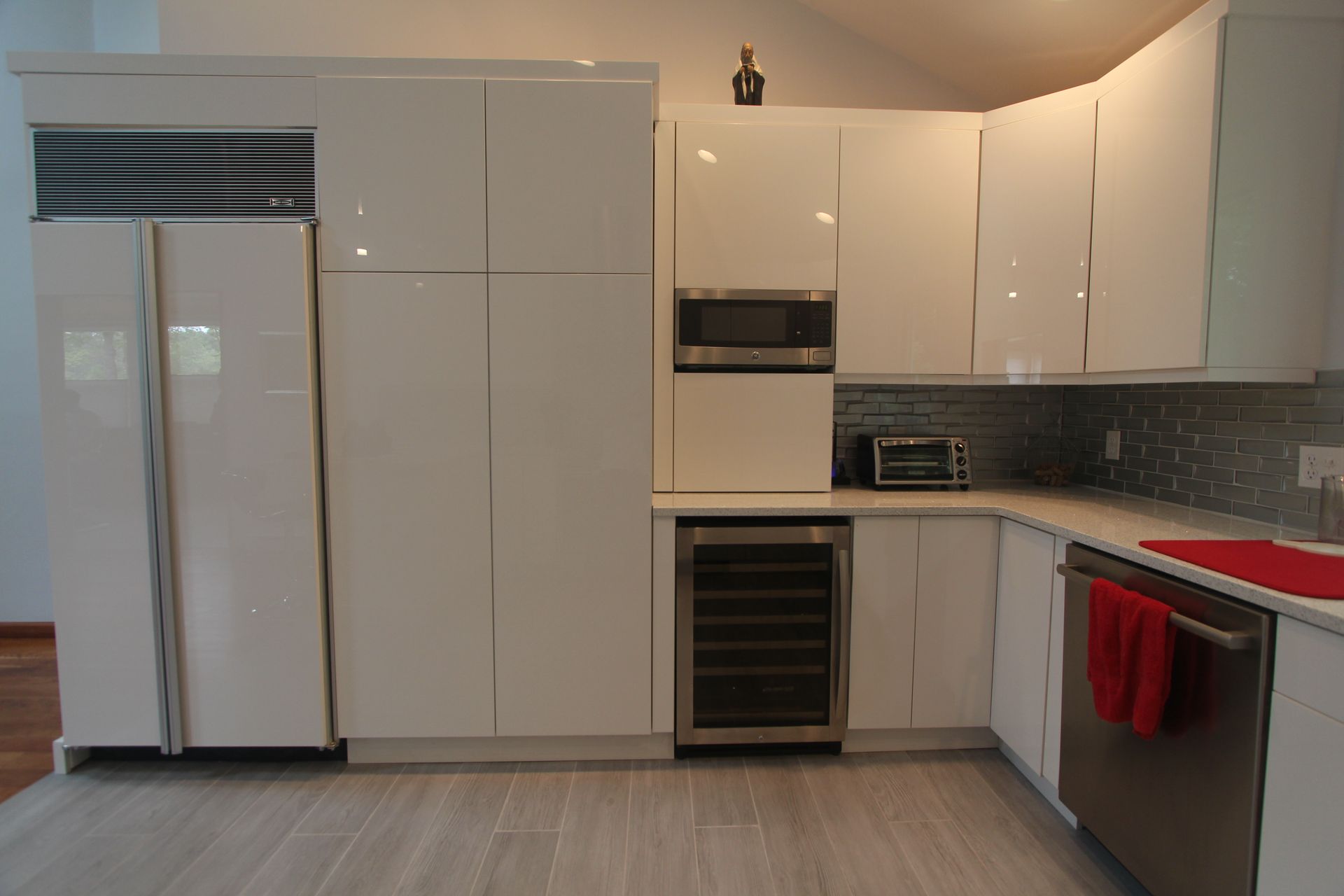 Modern kitchen with white cabinets, stainless appliances, gray backsplash, and red towels on a counter