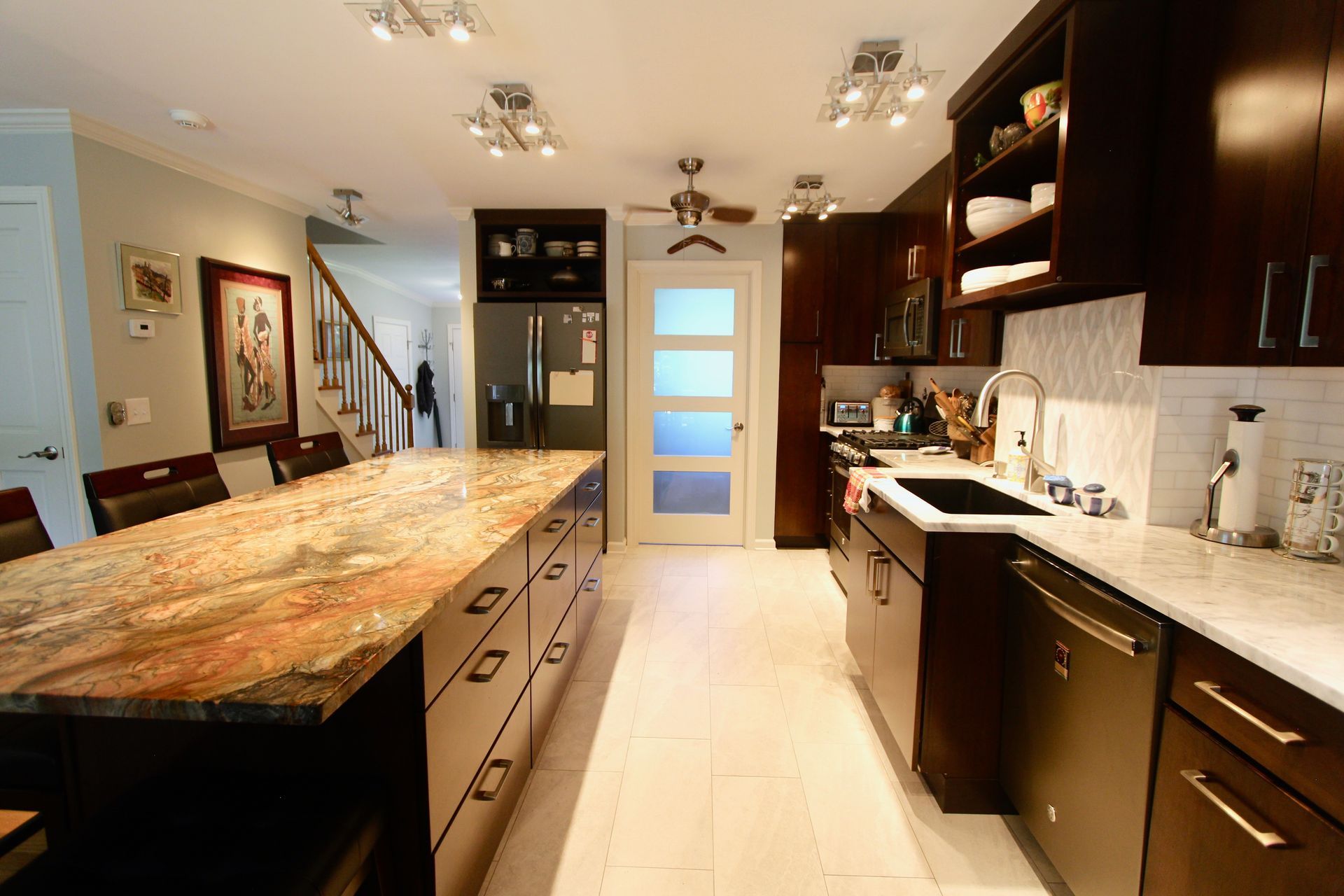 Modern kitchen with long island, dark wood cabinets, white counters, and bright ceiling lights