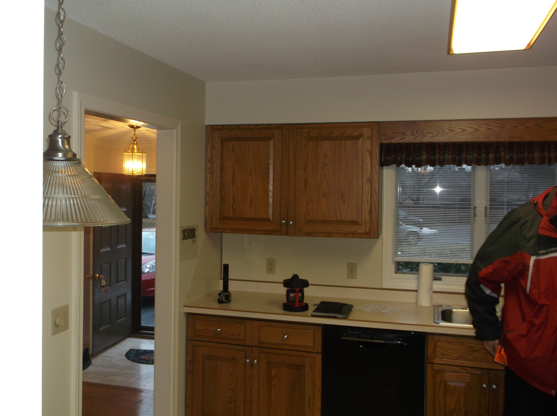 Kitchen with wood cabinets, countertop, sink, and window; hallway visible to the left.