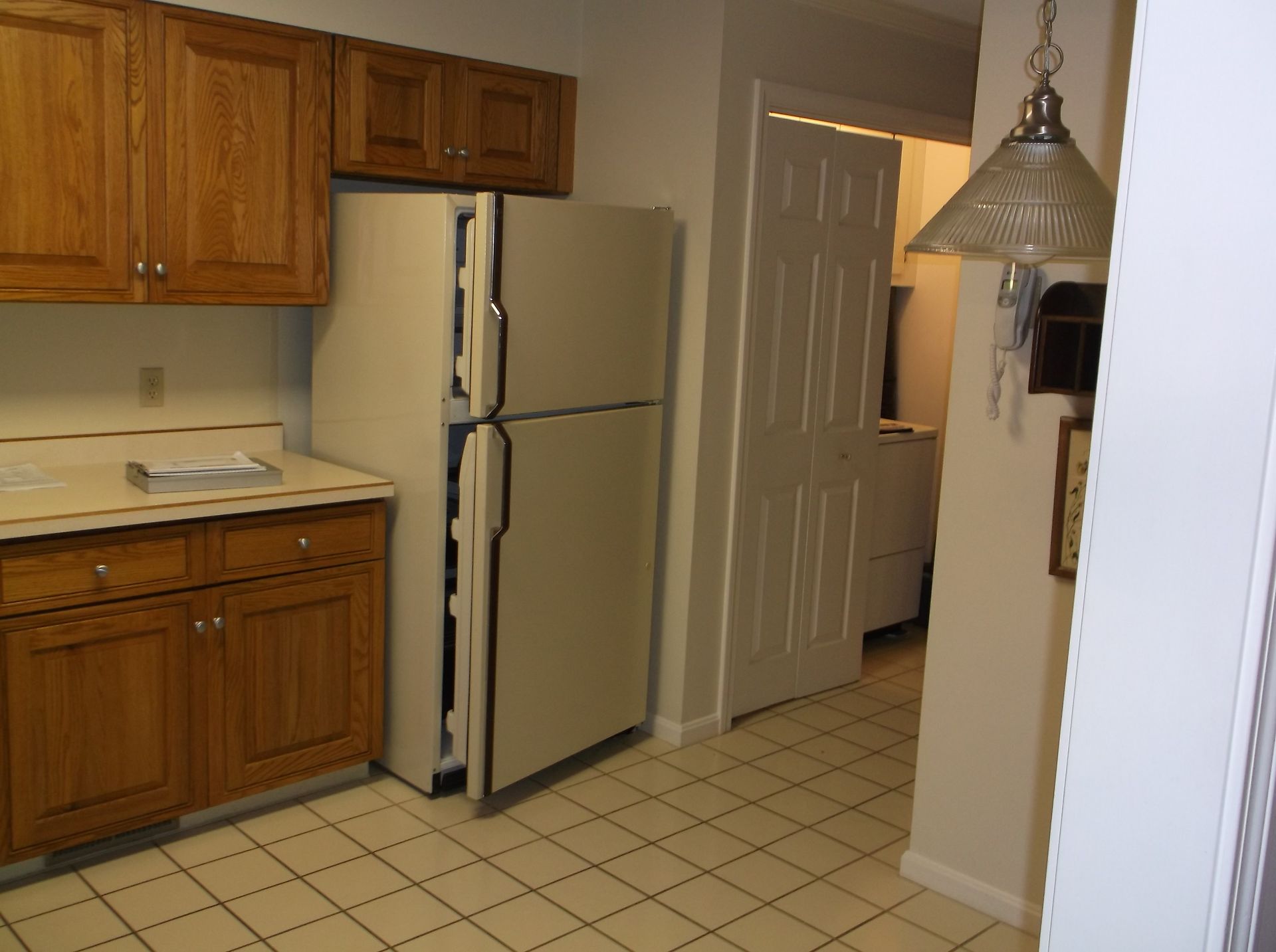 Small kitchen with wood cabinets, white refrigerator, tiled floor, and hanging pendant light.