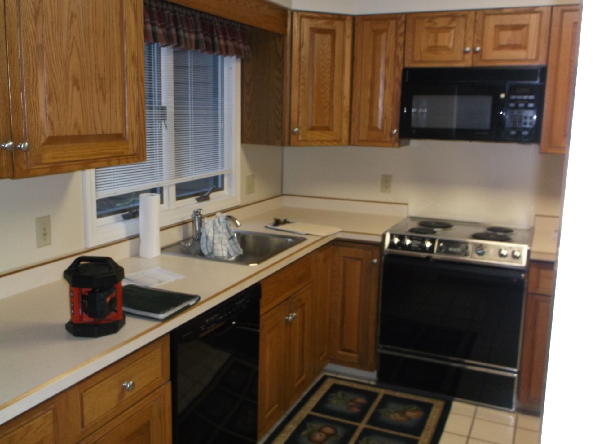 Small kitchen with wood cabinets, beige counters, sink by window, stove, microwave, and coffee maker.