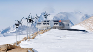 Snowy mountain facility with row of wind turbines and a small building under a clear sky