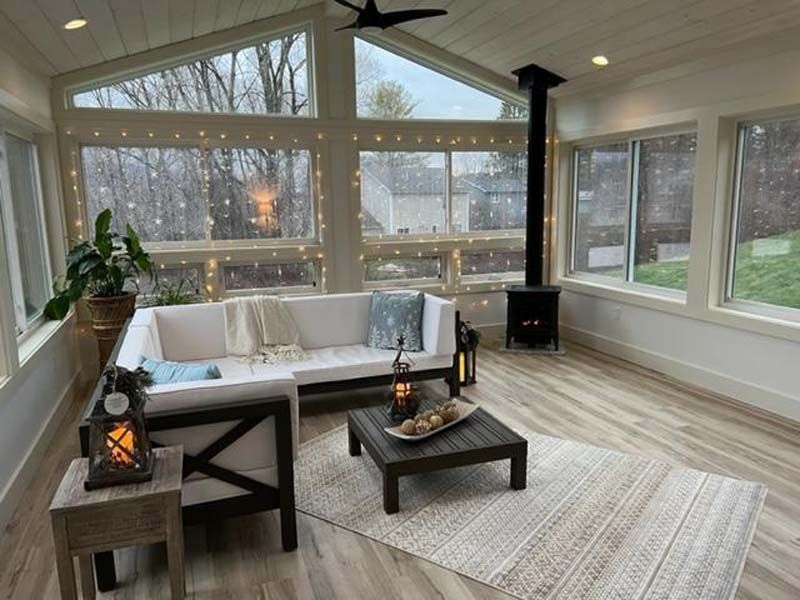 Sunroom with white sofa, dark coffee table, lanterns, large windows, and a light woven rug.