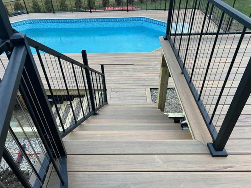 Wooden deck stairs leading down to a blue swimming pool with black railings.