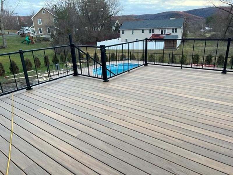 Spacious wooden deck with black railing overlooking a backyard and pool, with hills in the distance