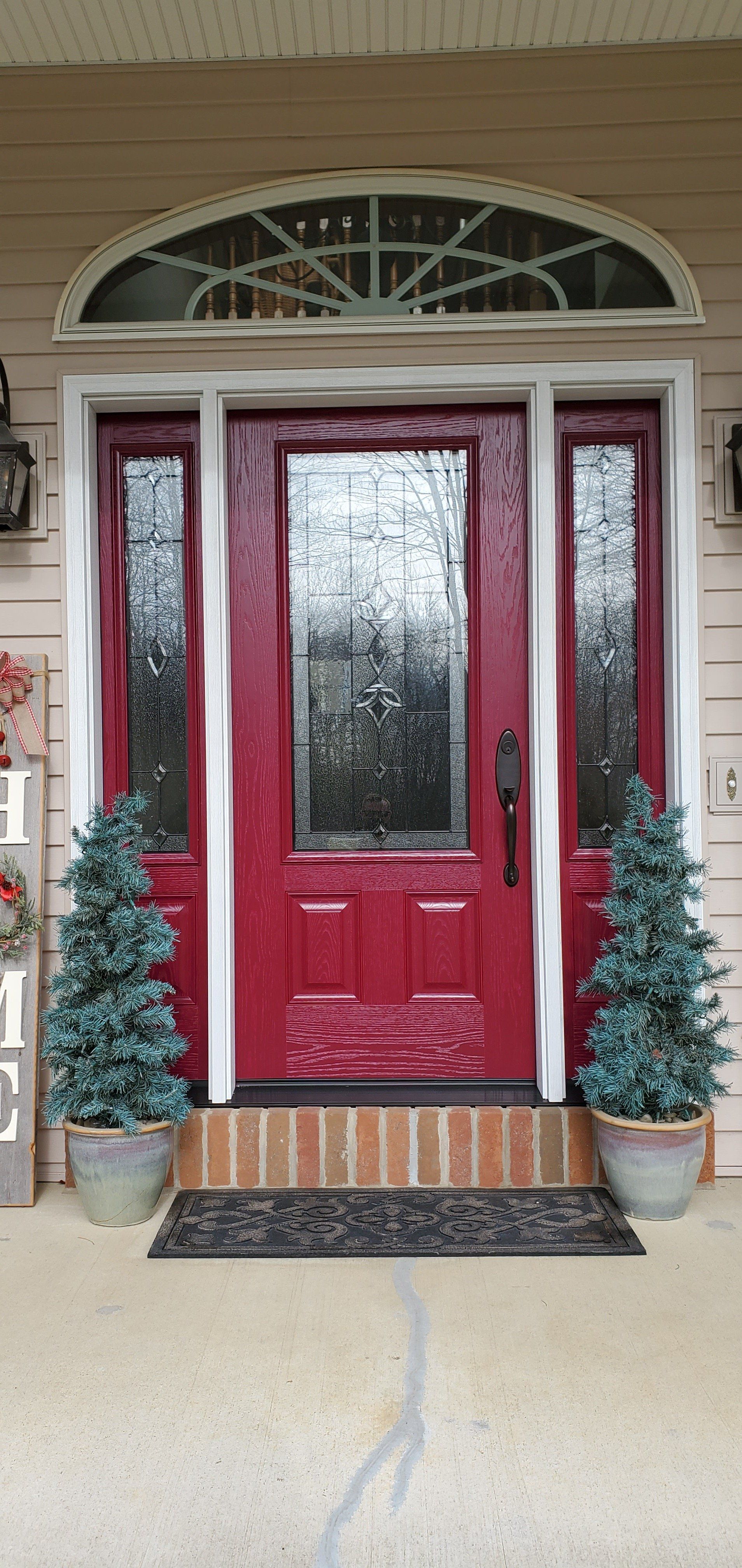 A red door with two christmas trees in front of it on a porch.