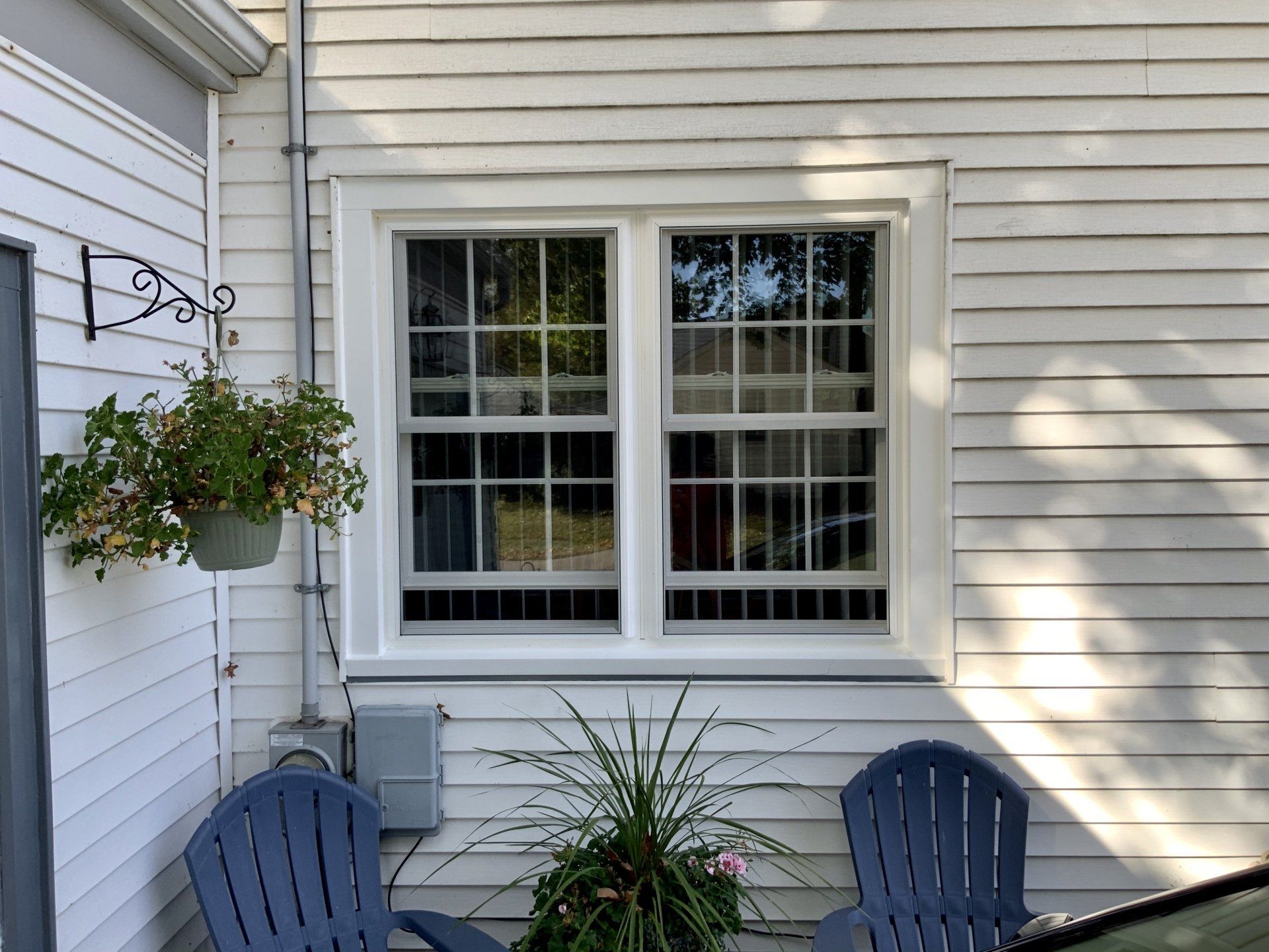 Two blue chairs are sitting in front of a window on the side of a house.