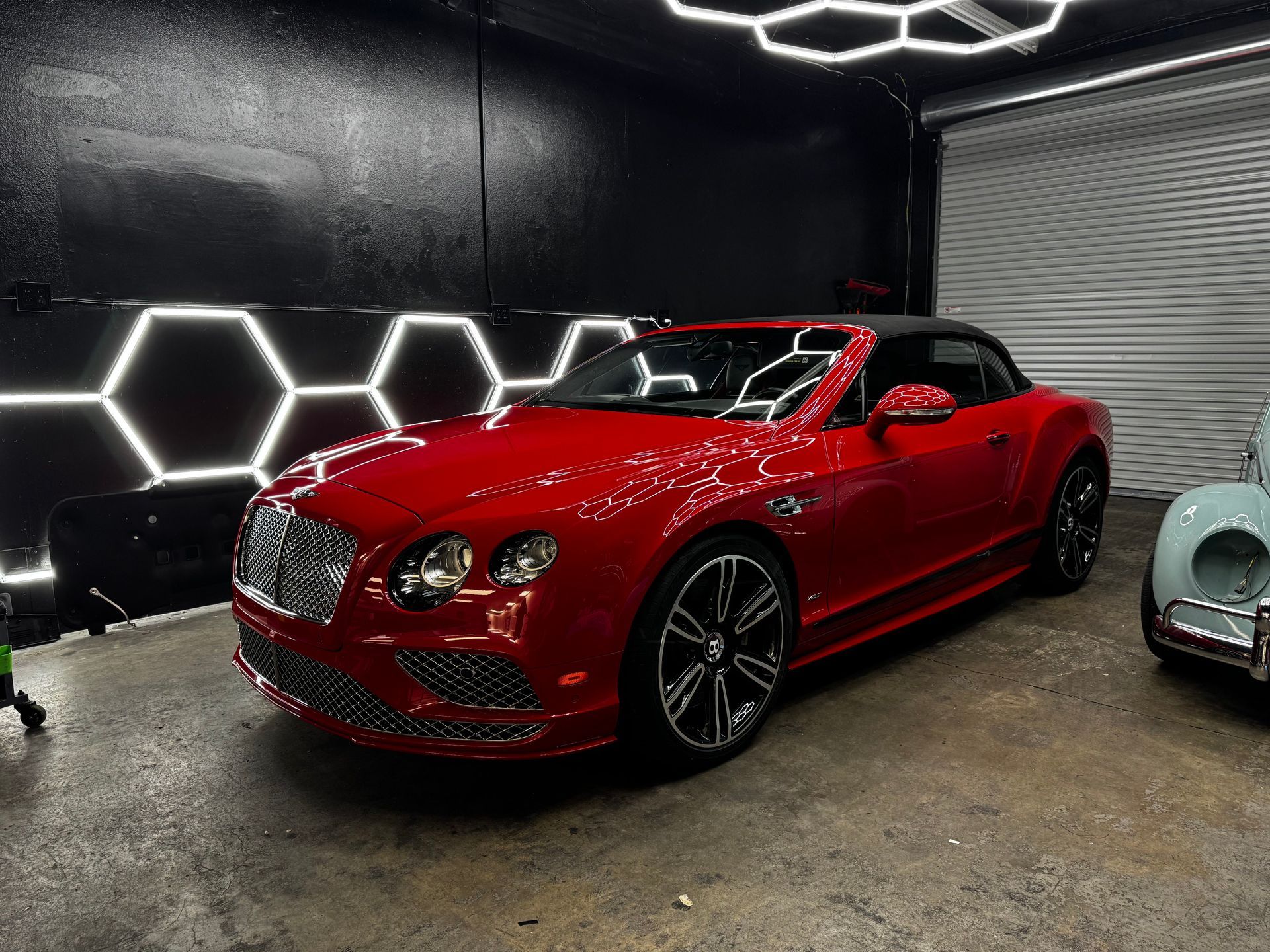 Red Bentley convertible in a black garage with hexagonal wall lights and a concrete floor.
