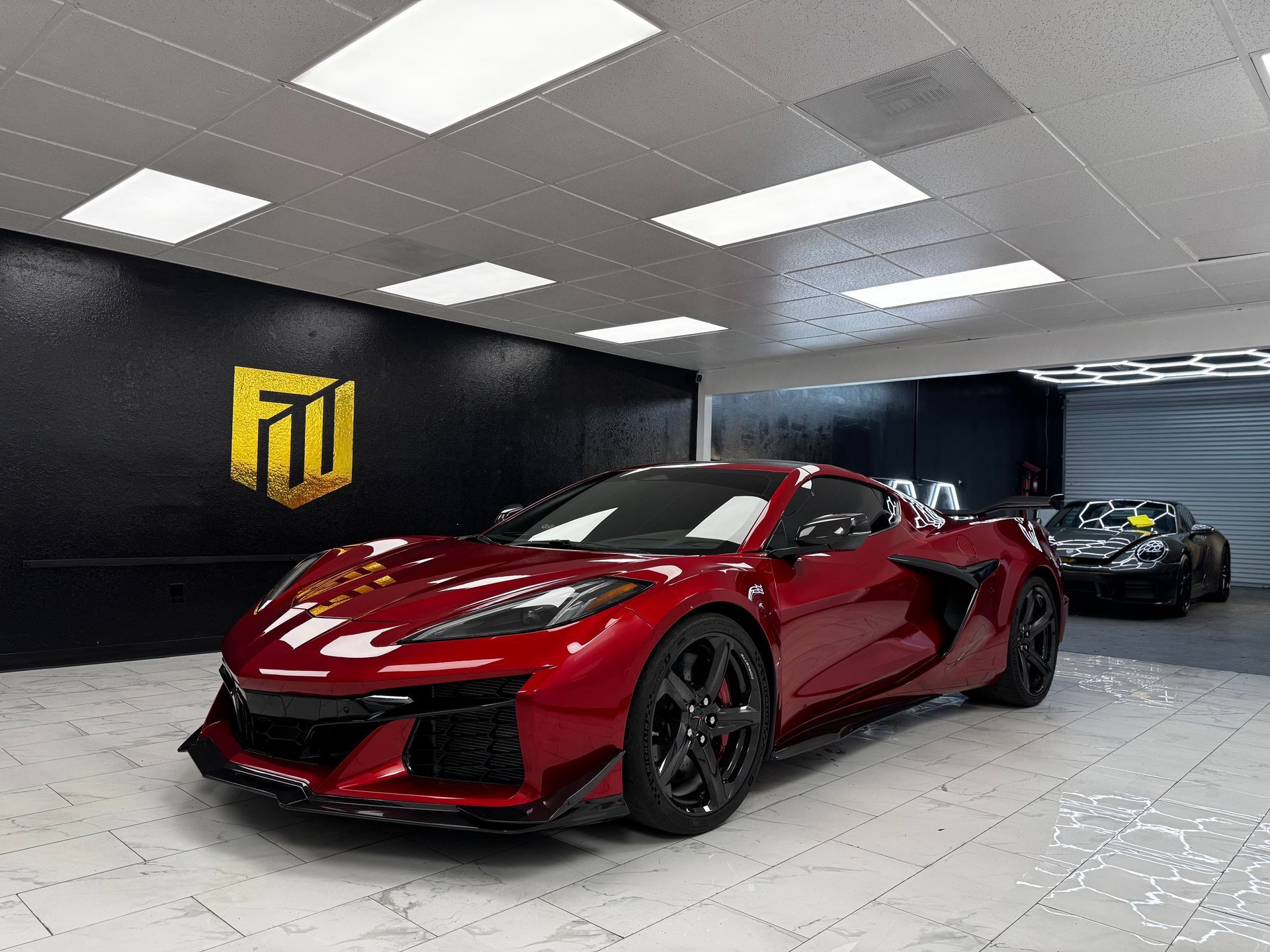 Red sports car in a modern showroom with a black-and-yellow logo on the wall and another car behind it