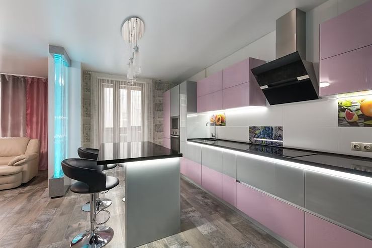 Modern kitchen with pink cabinets, black island stools, and a large window with sheer curtains.