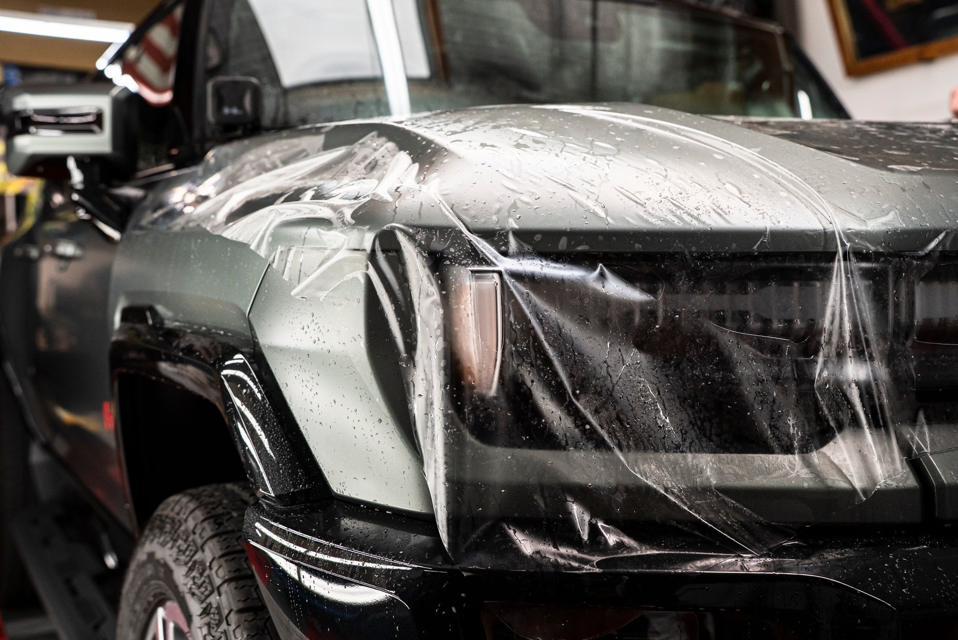 Silver sports car covered in protective film during detailing in a garage