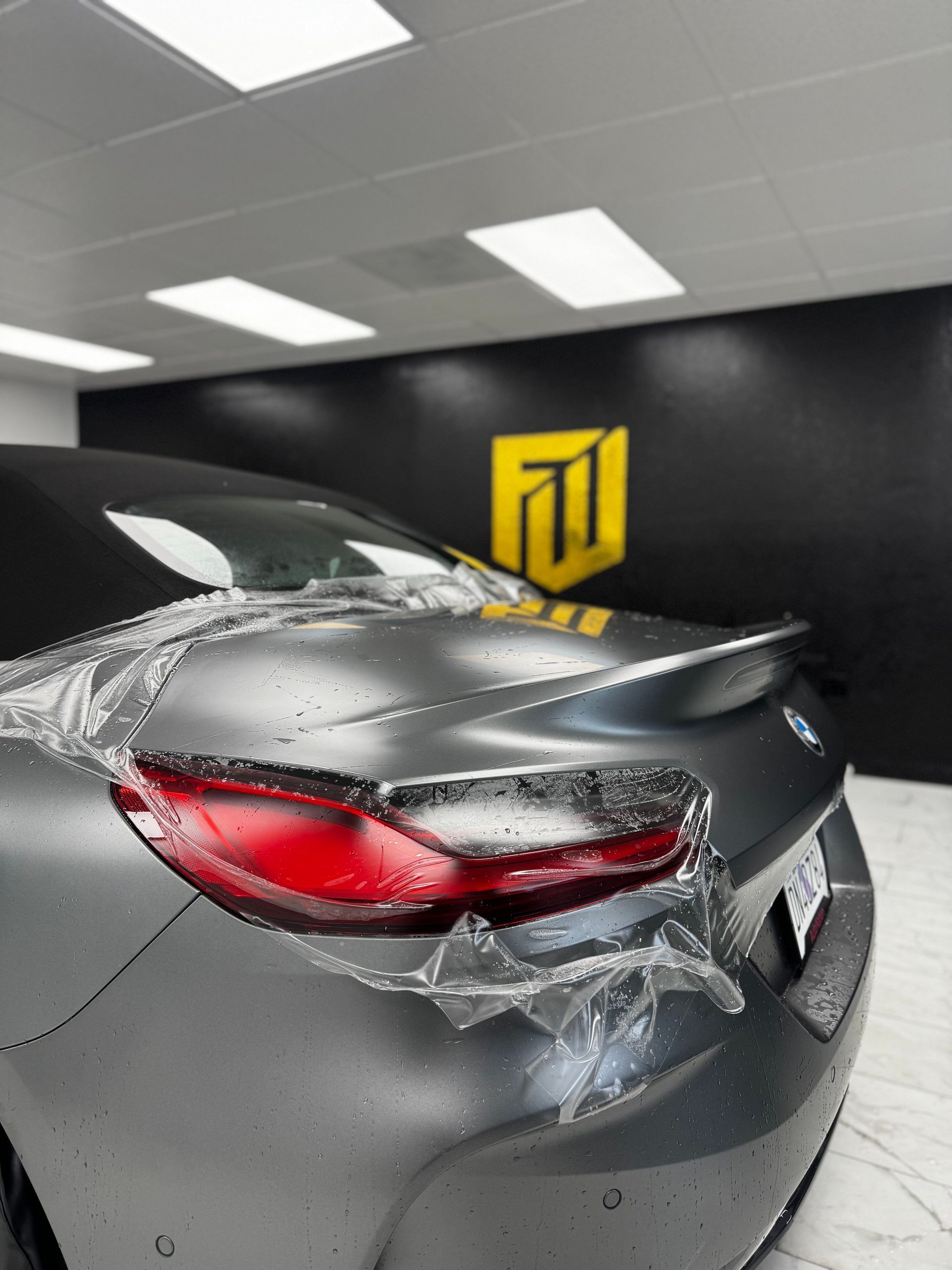 Rear view of a gray sports car with a shattered taillight in an indoor garage