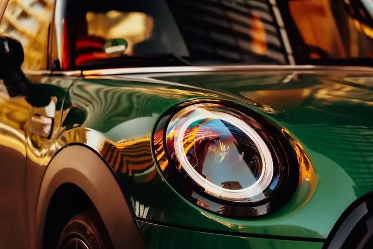 Close-up of a green Mini Cooper’s front headlight and hood in warm light