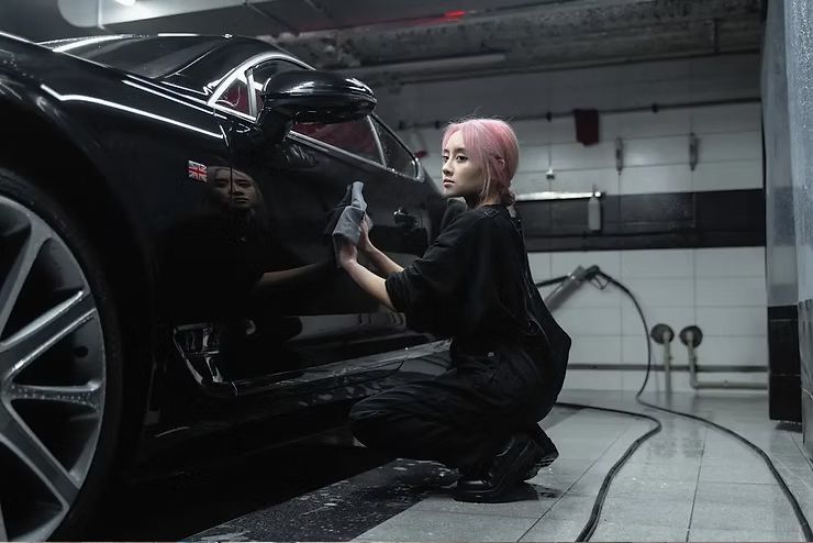 Person cleaning a black sports car in a garage, using a cloth and spray bottle
