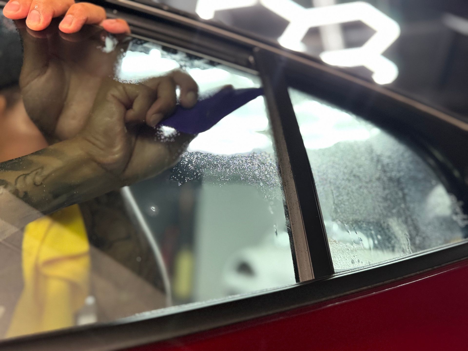 Hand polishing a car window with a cloth, showing water droplets and the car’s interior through the glass