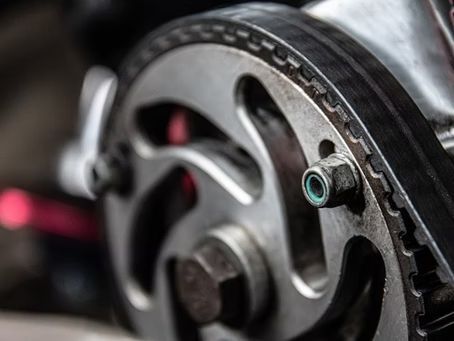 Close-up of a car engine timing belt and pulley system in metallic silver and black.