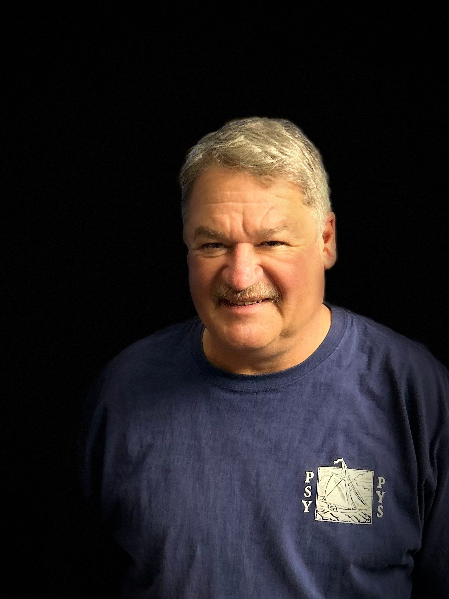 A man with a mustache is wearing a blue shirt and smiling.
