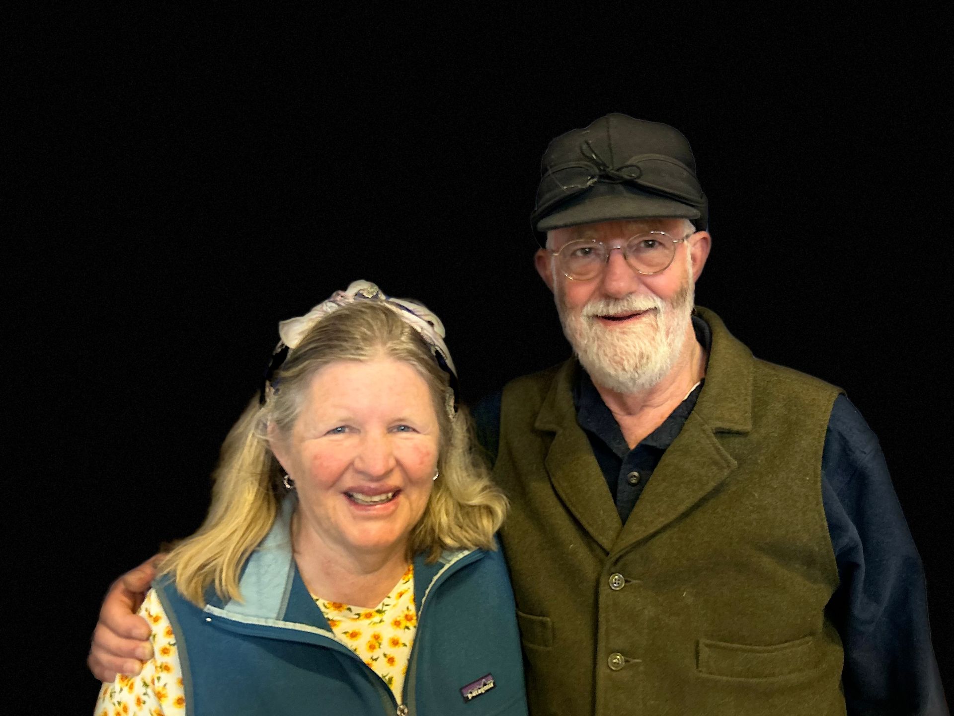 A man and a woman are posing for a picture in front of a black background.