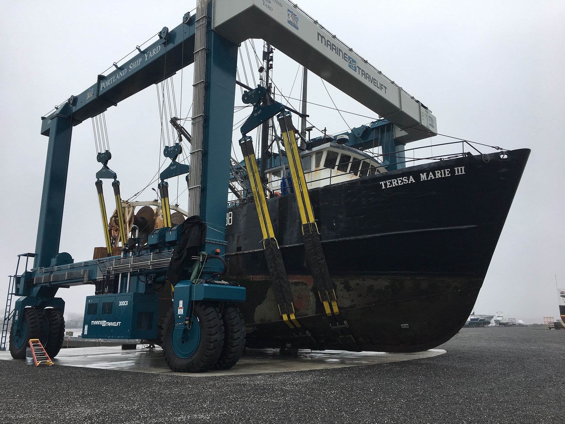 A large ship is being lifted by a large crane with the name tyran waste on it