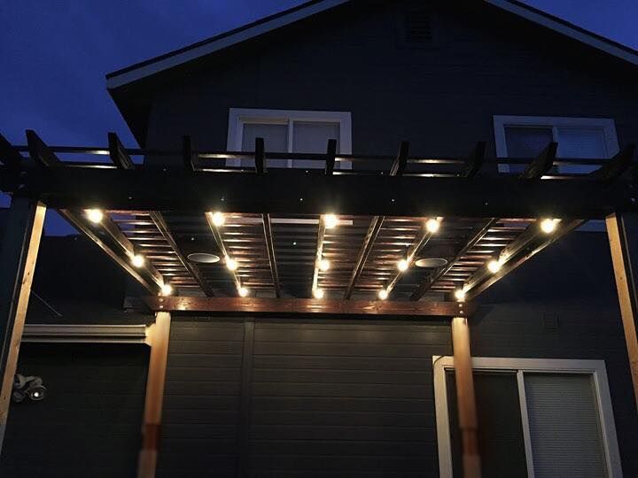 Pergola with string lights illuminating a dark house exterior at dusk.