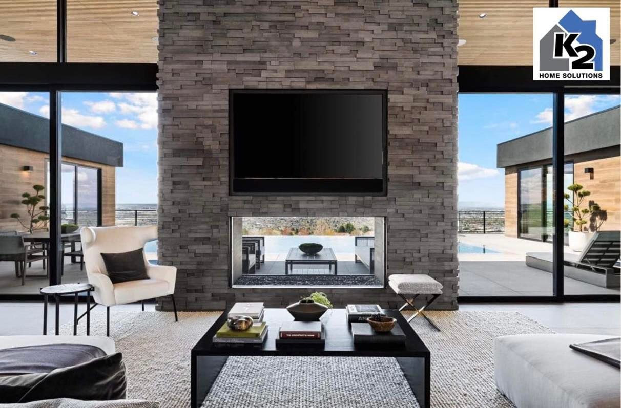 Living room with stone fireplace, TV, and large windows overlooking a pool and patio.