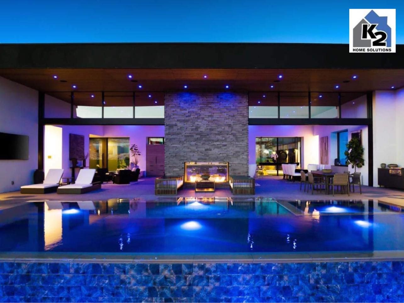 Luxury home exterior with a pool, lit with blue lights, and an outdoor fireplace.
