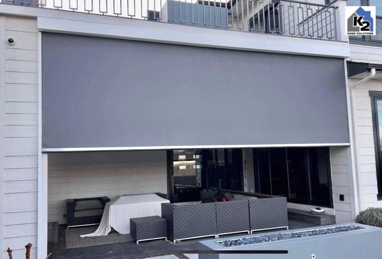 Gray outdoor retractable shade covers a patio with dark furniture.