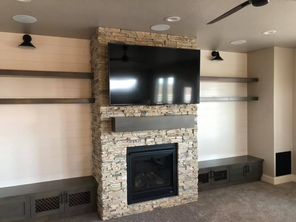 Stone fireplace with TV, floating shelves, and speakers in a neutral-toned room.