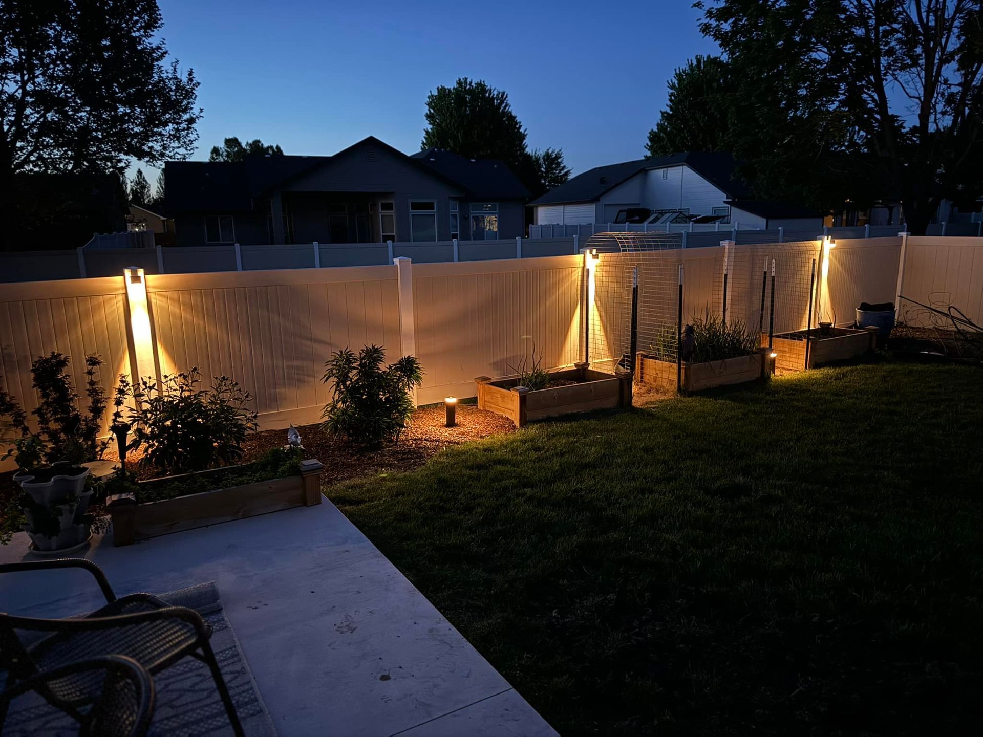 Backyard at dusk with lit fence and raised garden beds.