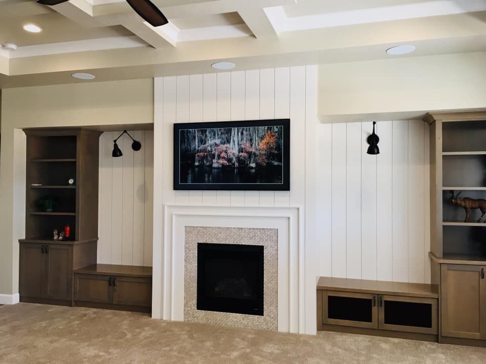 Living room with fireplace, built-ins, and TV mounted above the hearth. Walls are light-colored with white paneling.