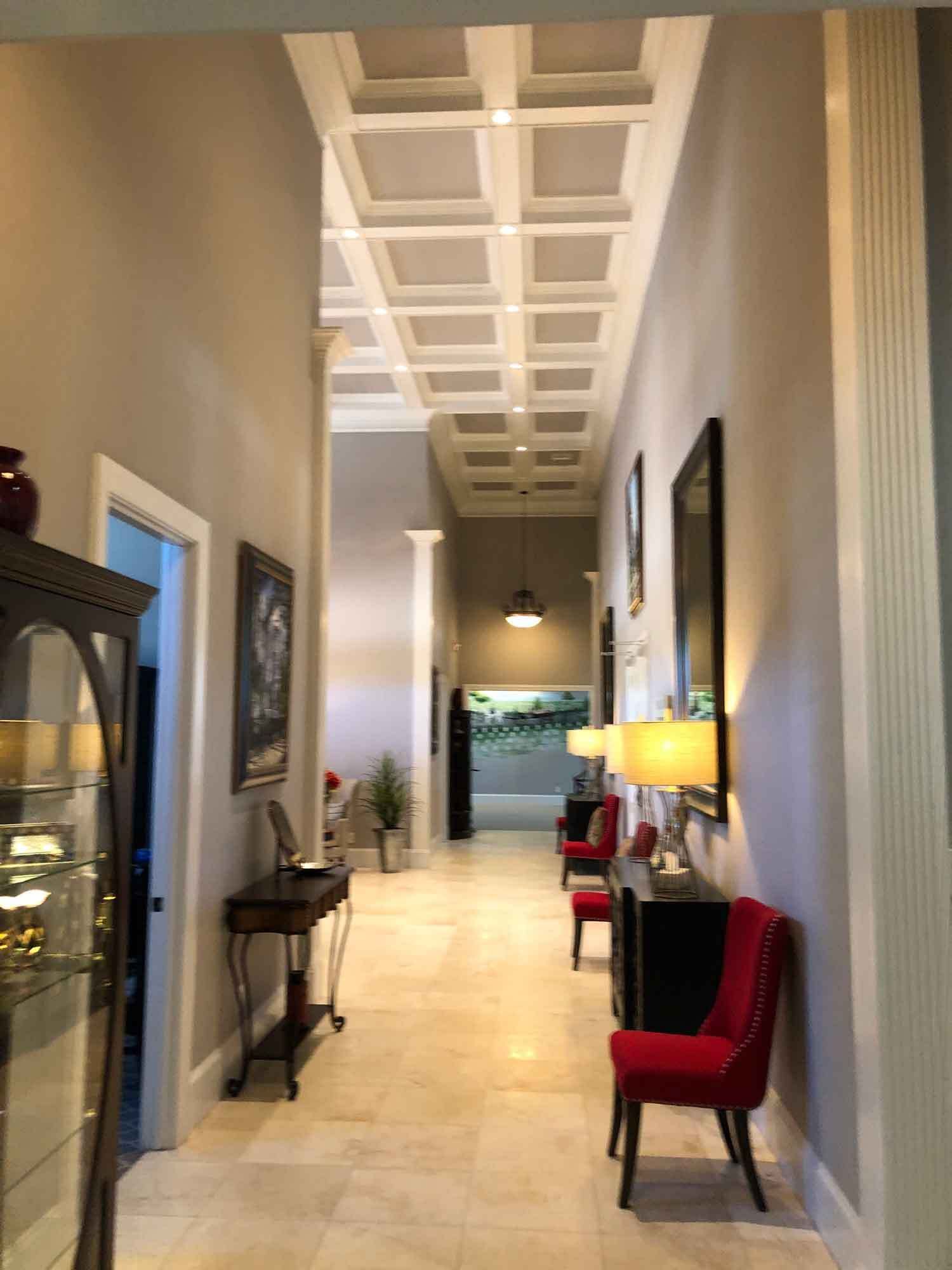 Long hallway with beige walls, coffered ceiling, and red chairs.