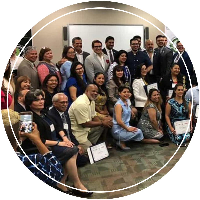 Group of diverse people pose together in a room, many holding certificates.  A whiteboard is in the background.