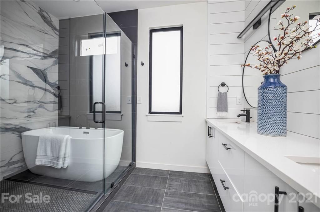 Modern bathroom with white cabinets, soaking tub, glass shower, marble accent wall, and vase of flowers.