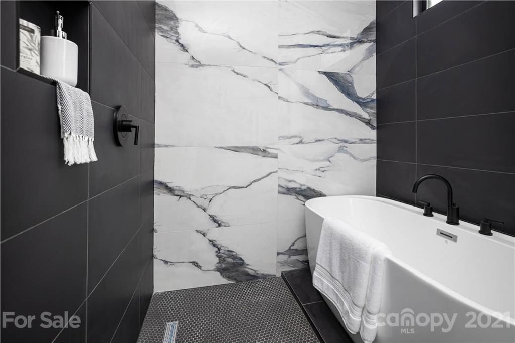 Bathroom with a white marble wall and black tiled walls, a bathtub, and fixtures.