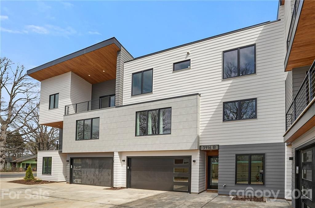 Modern multi-story townhomes with gray exteriors, dark windows, and garage doors. Blue sky.