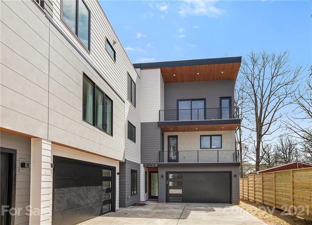 Modern three-story townhomes with gray and white siding, black garage doors, and balconies.