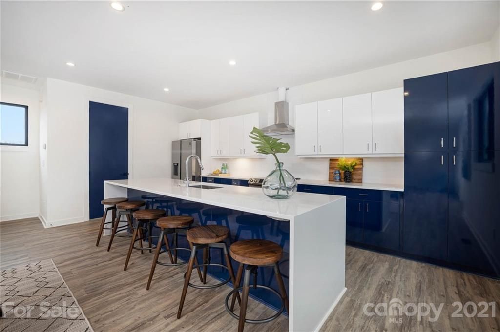 Modern kitchen with blue and white cabinets, large island with stools, stainless steel appliances, and wooden floors.