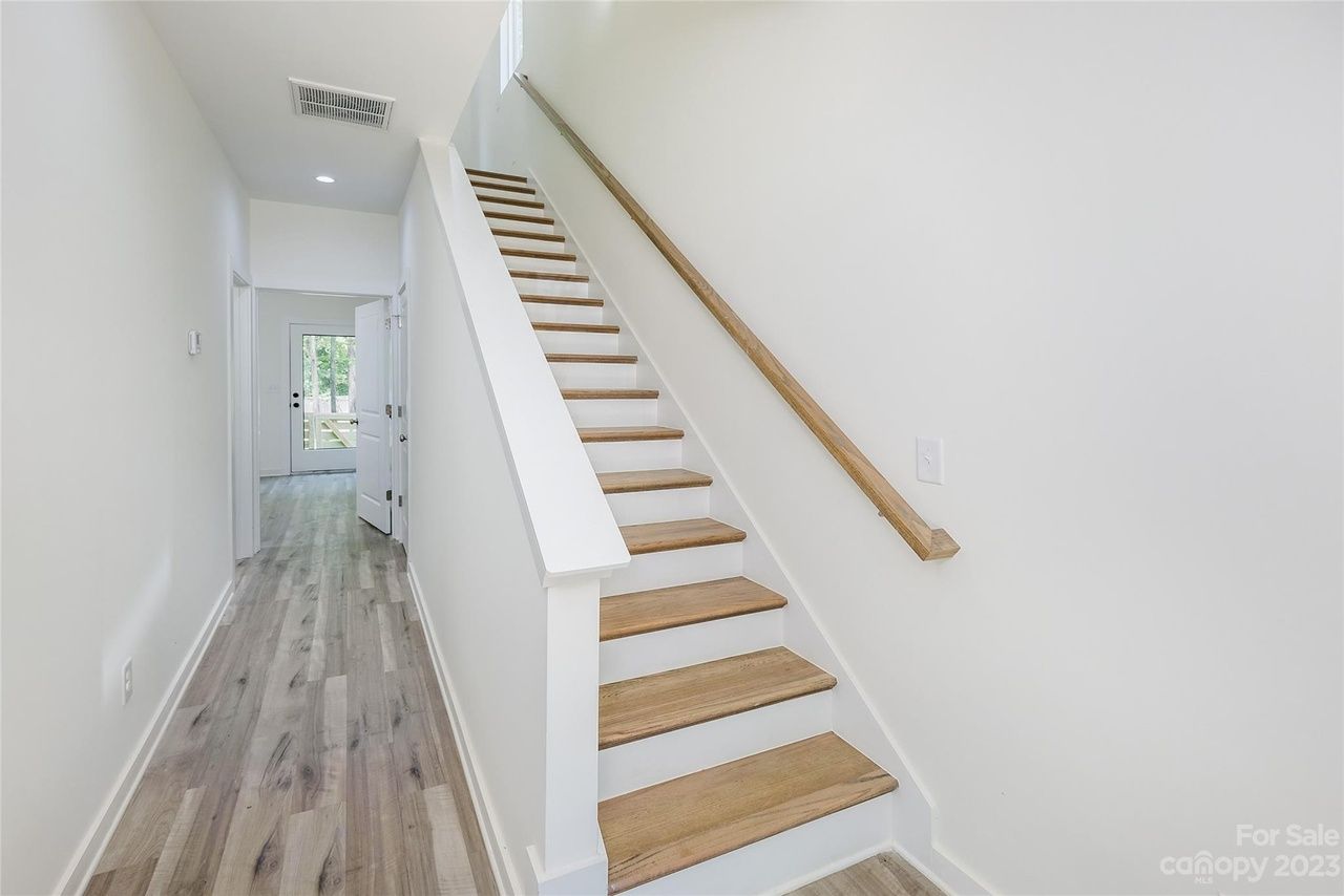 Hallway with wooden floor, stairs with light-colored treads, and a wooden handrail on the right.