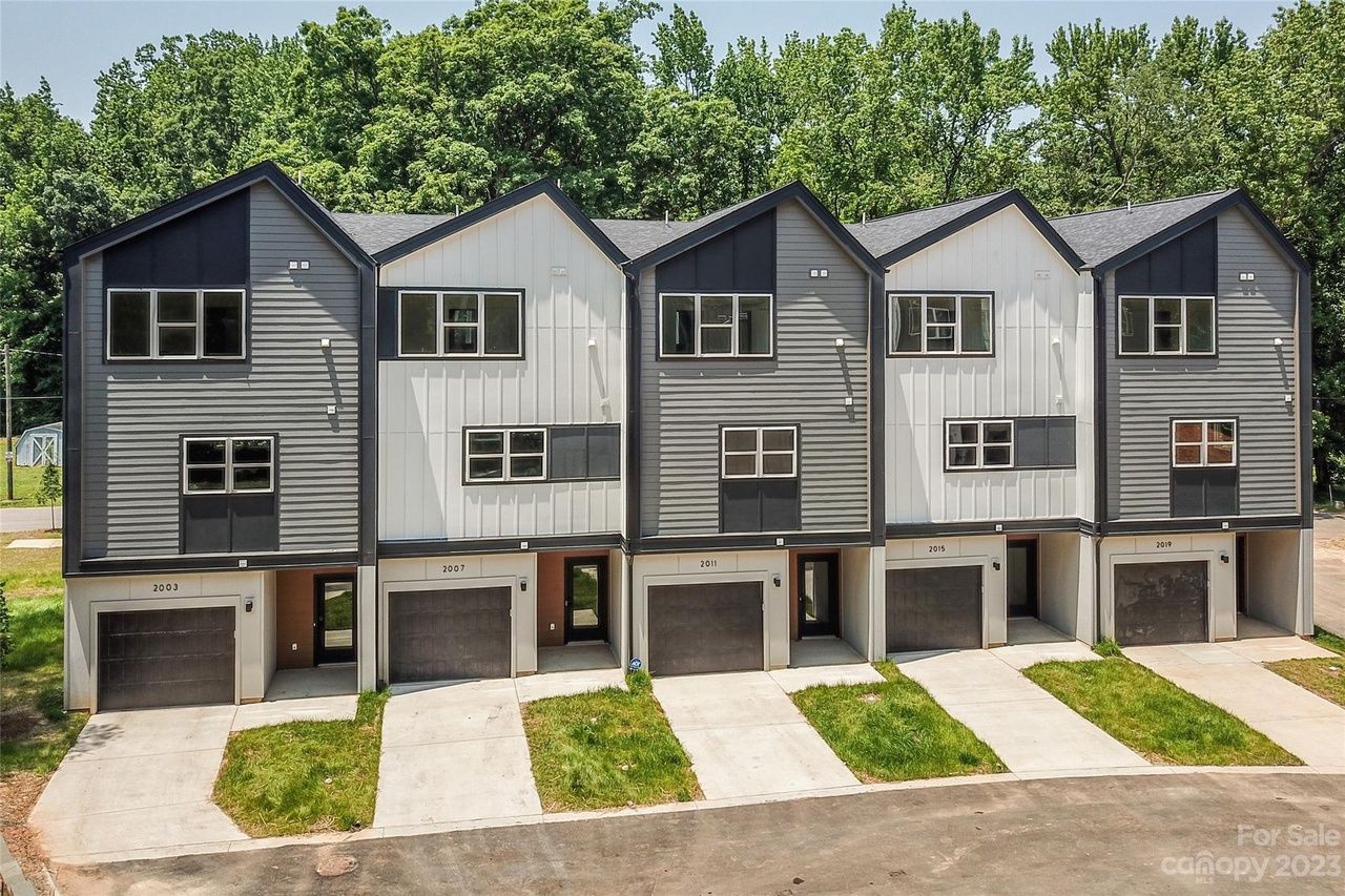 Row of modern townhouses with gray and white siding, black roofs, and garage doors.