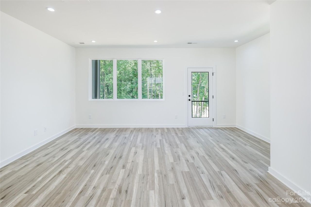 Empty room with light wood flooring, white walls, large window, and door to a balcony.