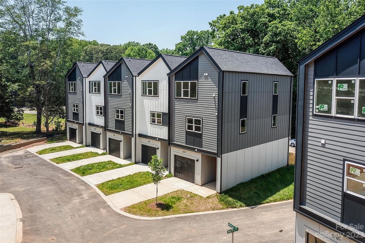 Row of modern townhouses with dark gray siding, white trim, and garages, on a sunny day.