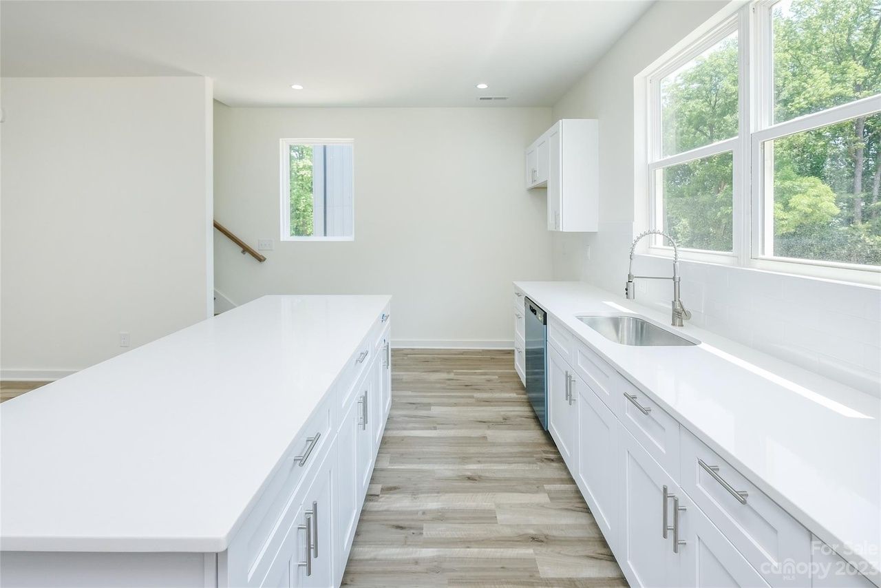 Bright, white kitchen with long island and countertops, wood floors, and large windows.
