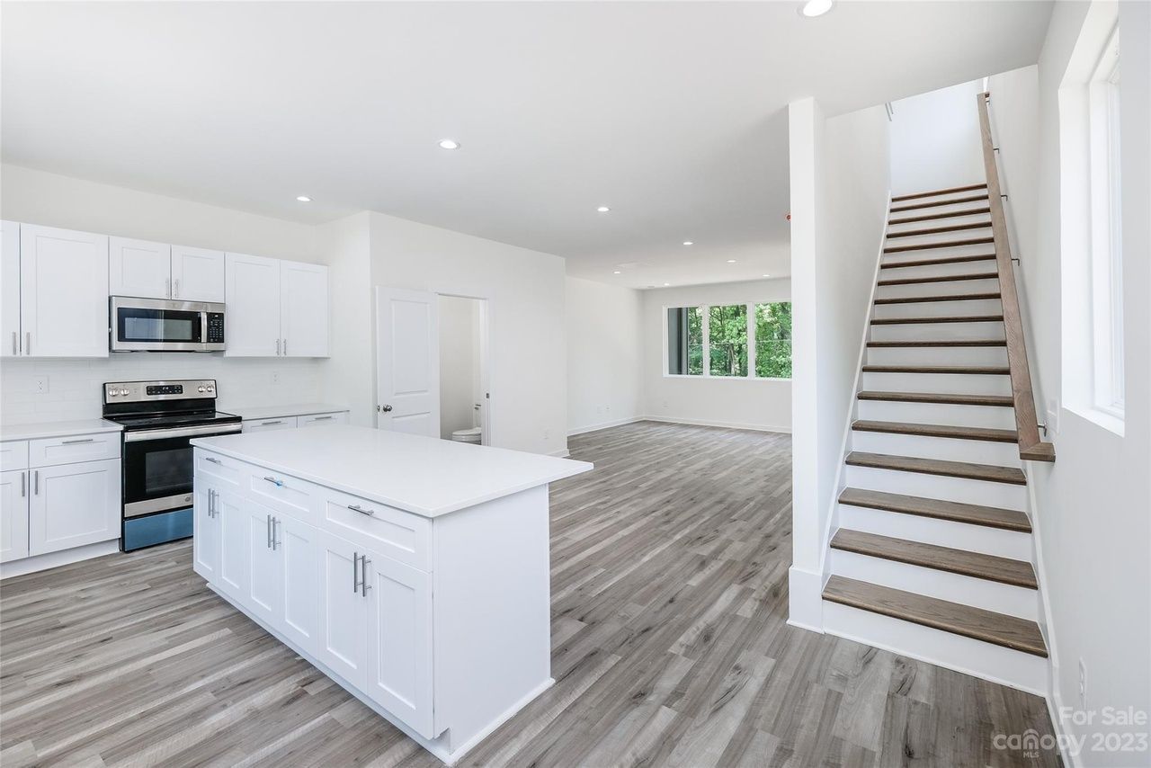 Bright white kitchen with island, stainless steel appliances, and staircase.