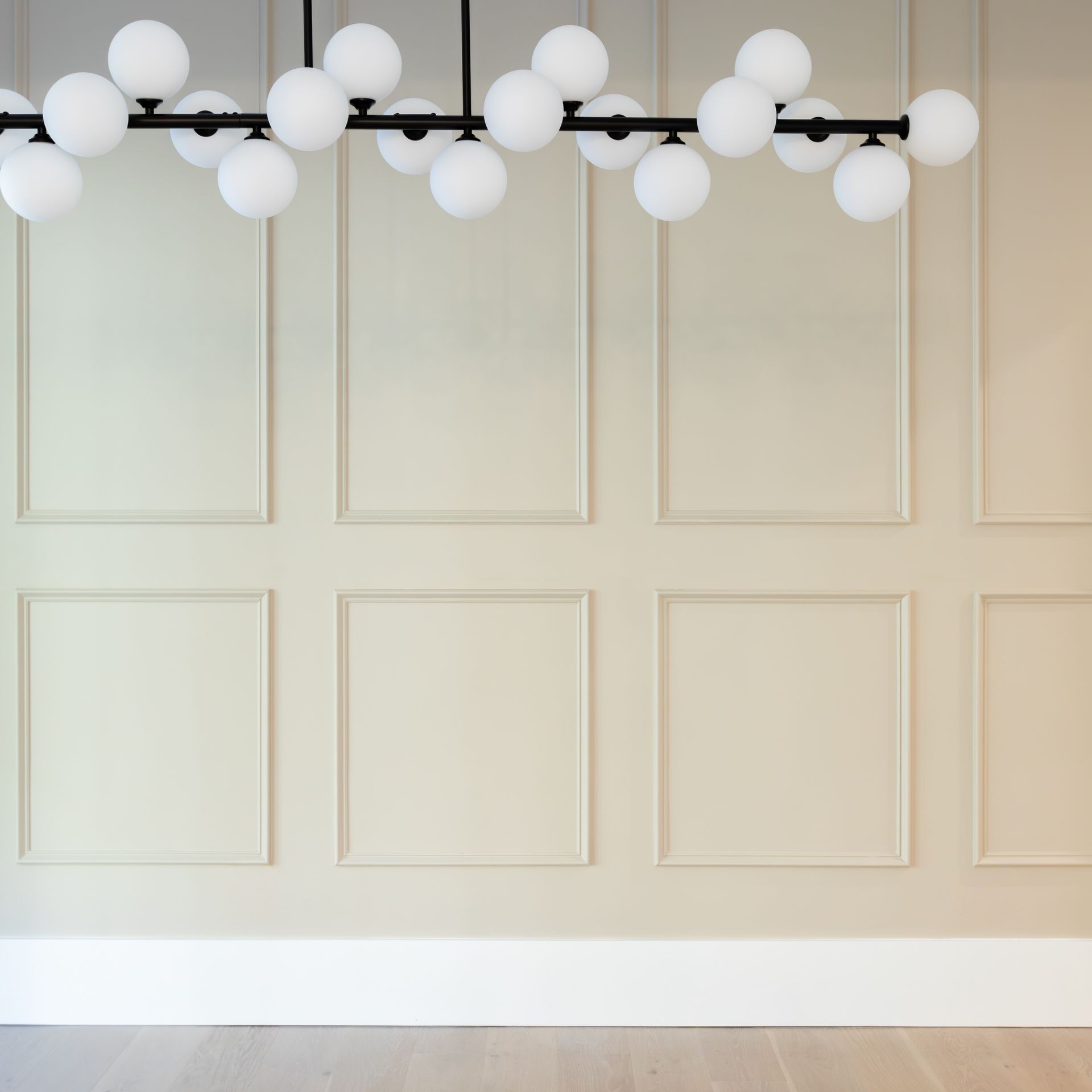 Modern light fixture with globe bulbs above a cream-paneled wall and white baseboard.