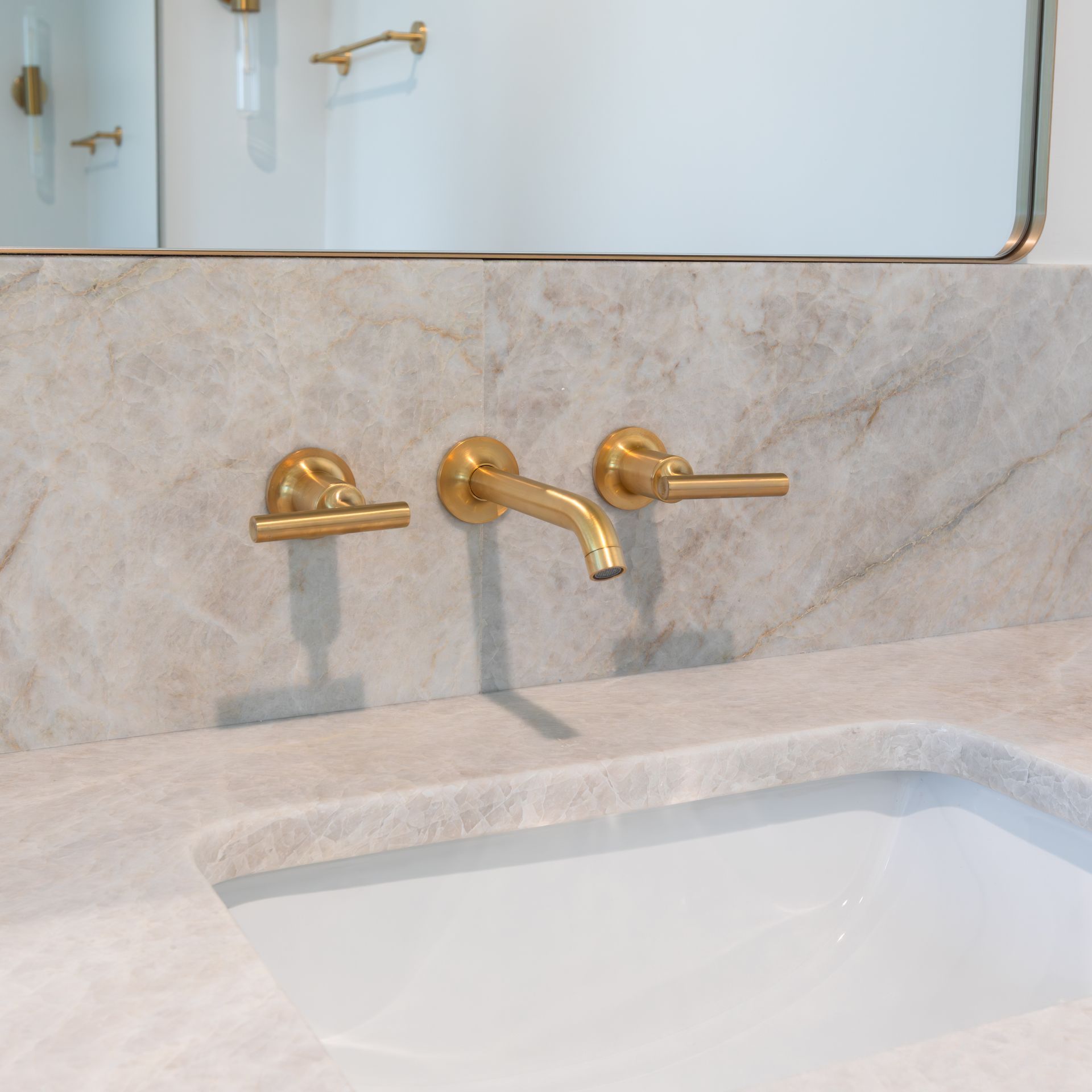 Gold faucet and handles on a marble backsplash above a white sink.